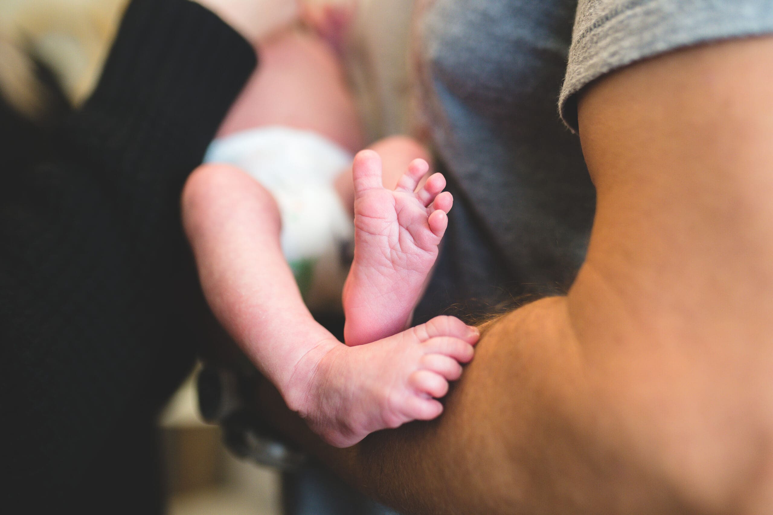 Close-up of a newborn baby's tiny feet cradled in strong arms, symbolizing the journey of fertility, sperm health, and the miracle of life after vasectomy reversal.