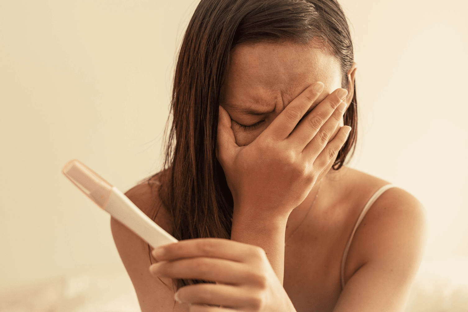 A woman holding a negative pregnancy test with her face in her hand, expressing deep emotion and disappointment.