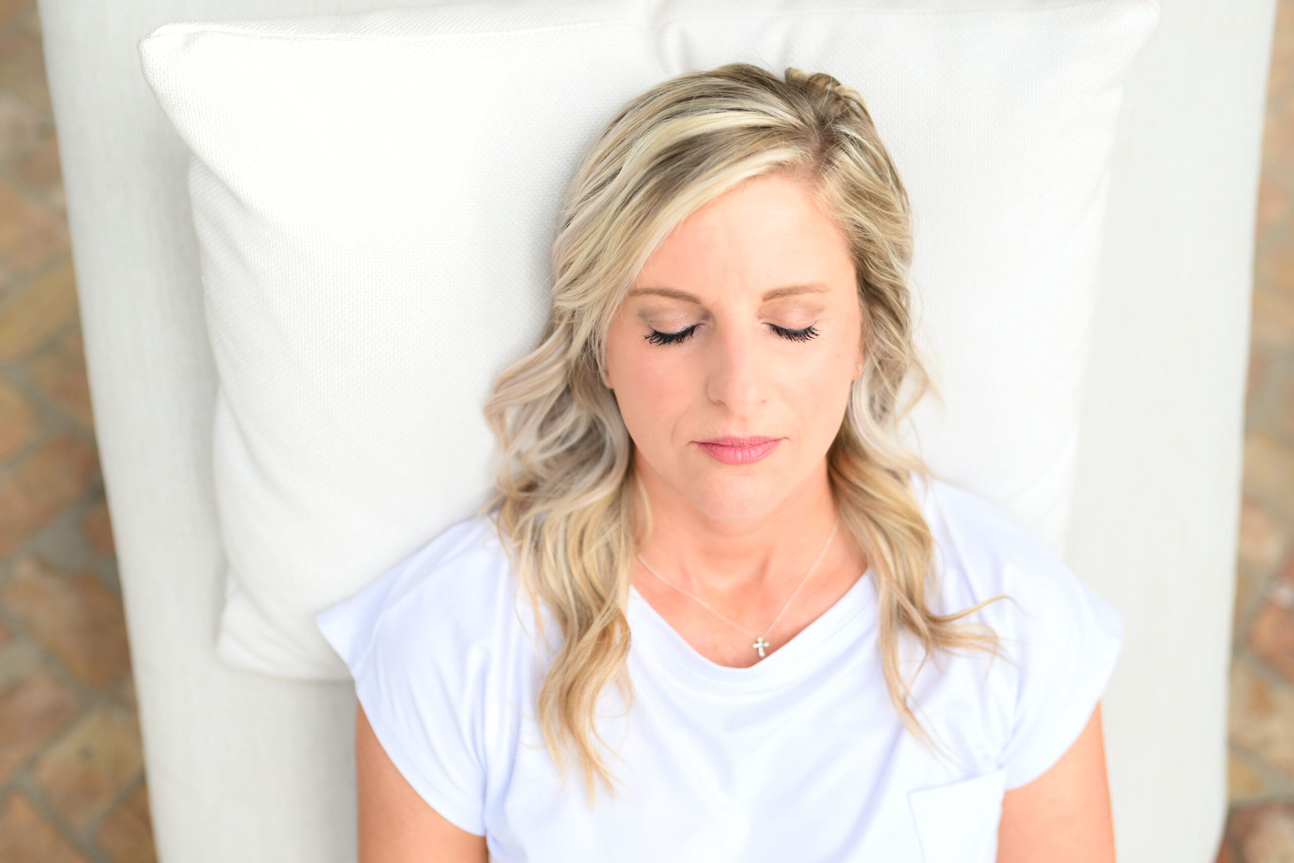 Woman with blonde hair lying on a white pillow with eyes closed, appearing relaxed and peaceful, symbolizing the importance of rest for fertility.