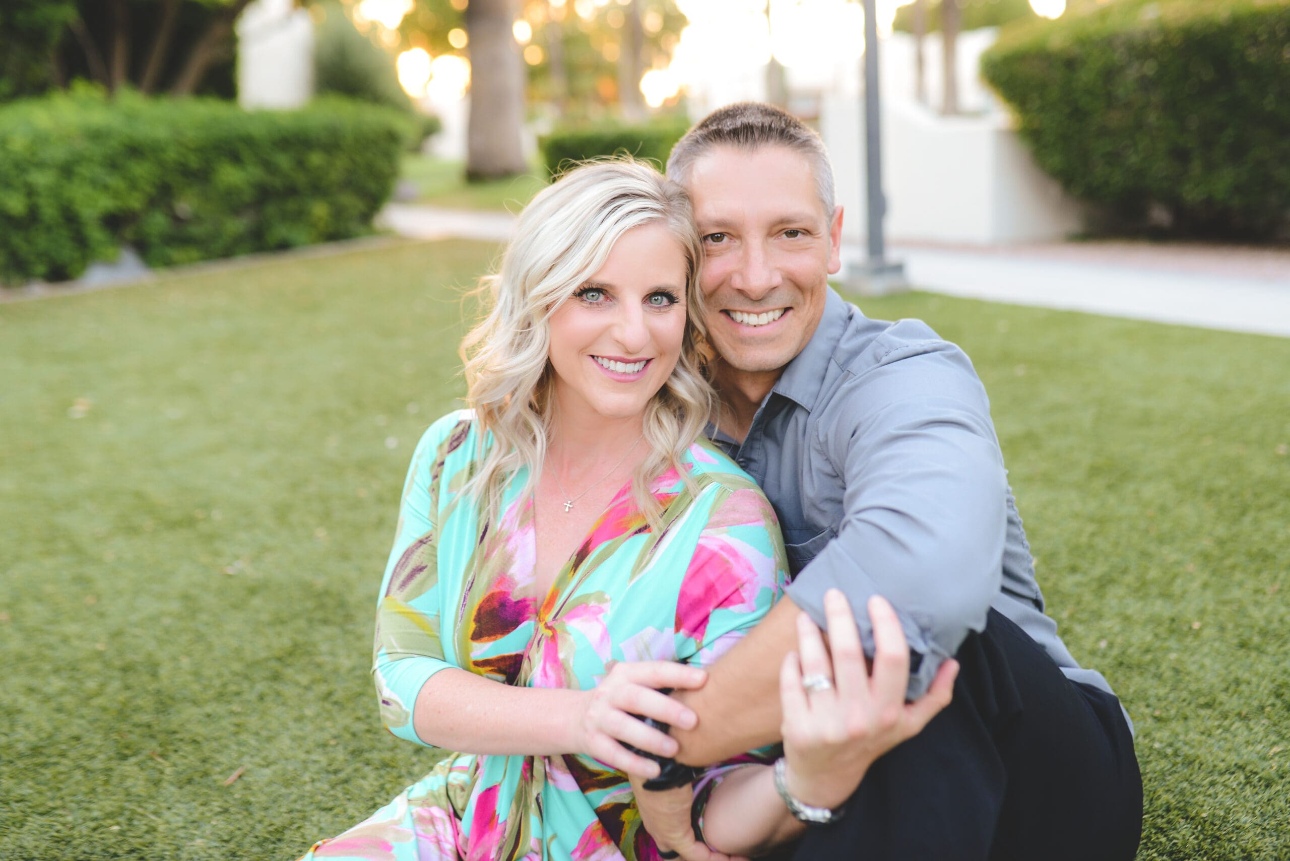 A happy couple sitting on a lush green lawn, embracing with smiles. The woman, in a floral dress, and the man, in a gray shirt, reflect love, faith, and connection while navigating the emotional journey of fertility struggles.